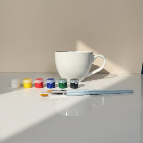Zestaw DIY do malowania – duża porcelanowa filiżanka, farby i pędzle.